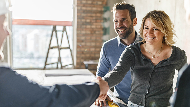 A woman shaking a contractors hand. A man is behind her. Both are smiling.