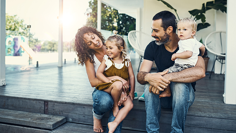 A mother and father sitting on a deck. Each has a child in their lap.